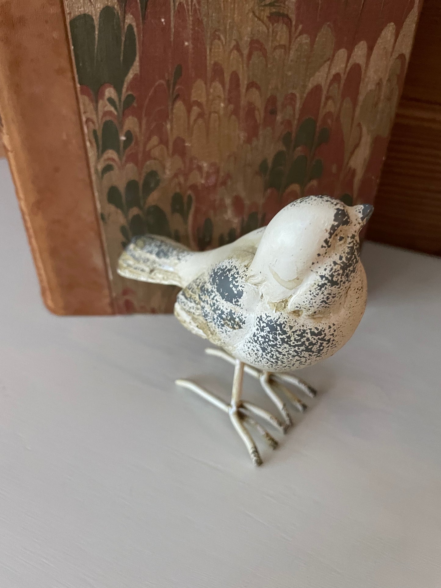 Top view of distressed white/grey resin metal bird decor on vintage books. A unique and rustic home accent for cozy and elegant interiors.