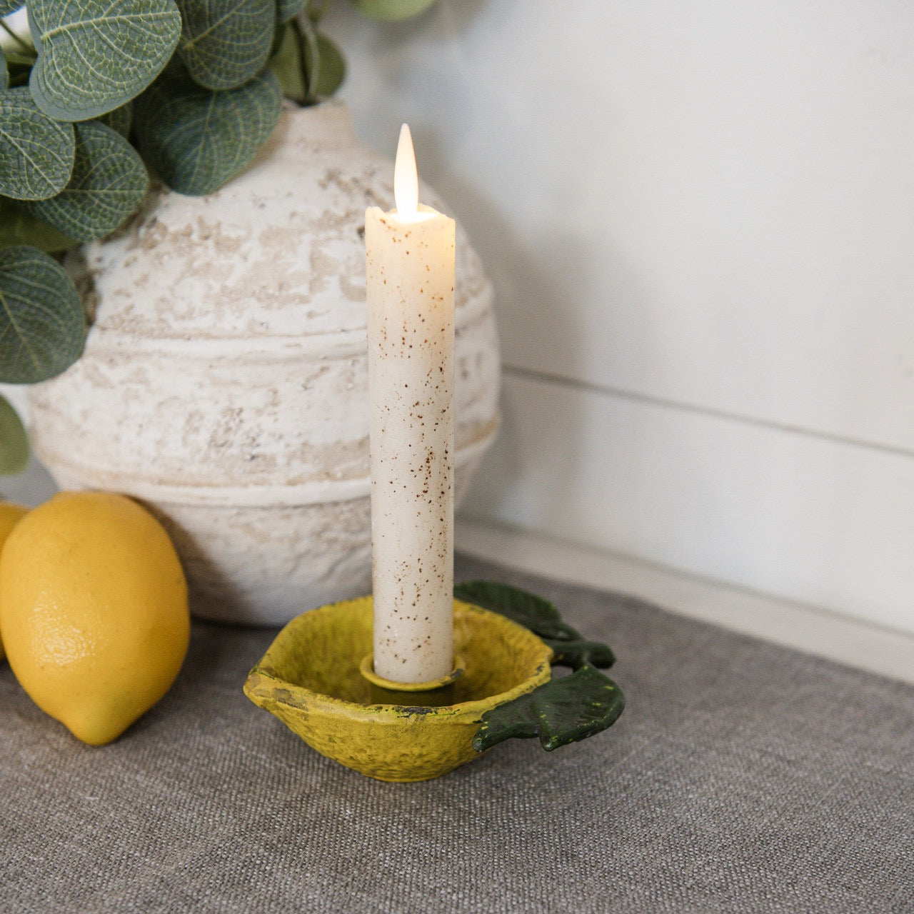 Lemon taper candle holder with a lit candle, styled on a tabletop with lemons and greenery, creating a cozy and fresh home decor accent.