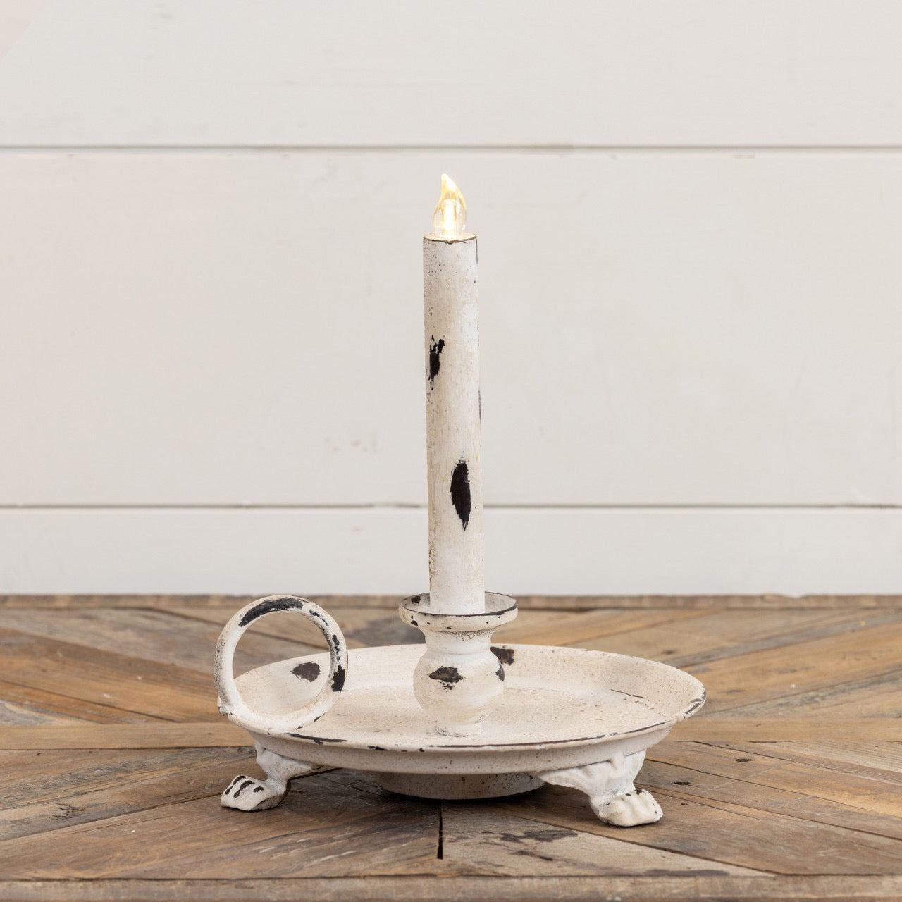 White metal dish taper candle holder with an antique distressed look, clawfoot legs, and a side handle. Ideal for farmhouse and rustic home decor.