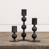 Collection of three black metal sculpted taper candlesticks in varying heights. Elegant candle holders for sophisticated home decor.