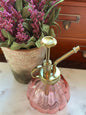 Chic pink glass plant mister with brass nozzle, perfect for precise watering. Stylish home decor accessory for plant care and hydration.