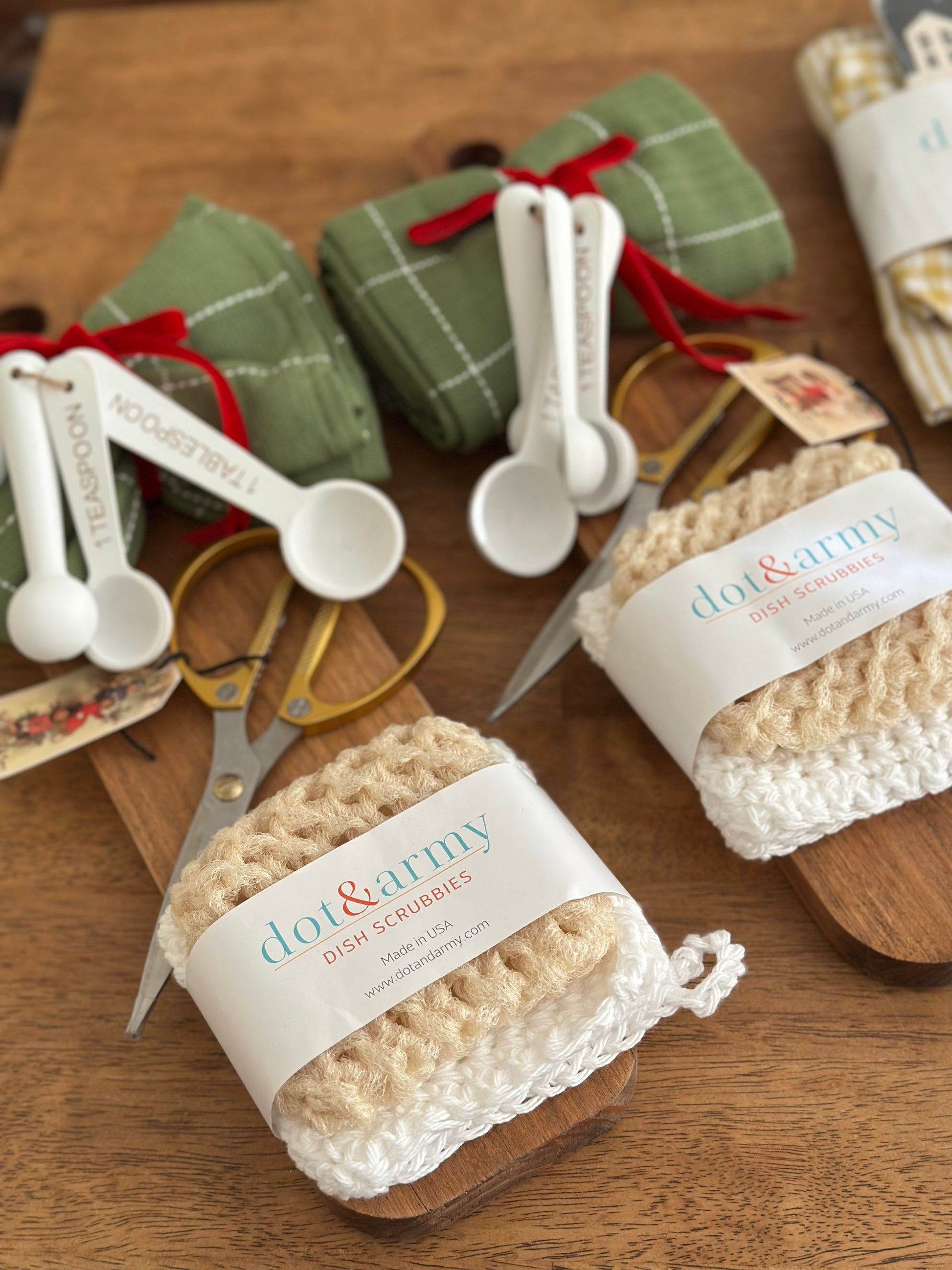 Dot & Army dish scrubbers with measuring spoons and plaid paper on a wooden surface