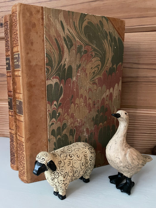 Resin goose and sheep figurines displayed beside vintage books. Unique home decor pieces for collectors and rustic-themed interiors.