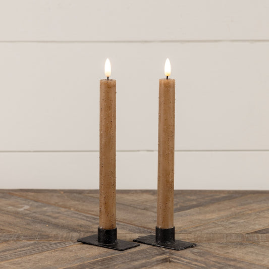 Set of two 9.5-inch beige taper candles with realistic 3D flame effect, placed on black metal holders on a wooden surface. Perfect for home decor.