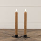 Set of two 9.5-inch beige taper candles with realistic 3D flame effect, placed on black metal holders on a wooden surface. Perfect for home decor.
