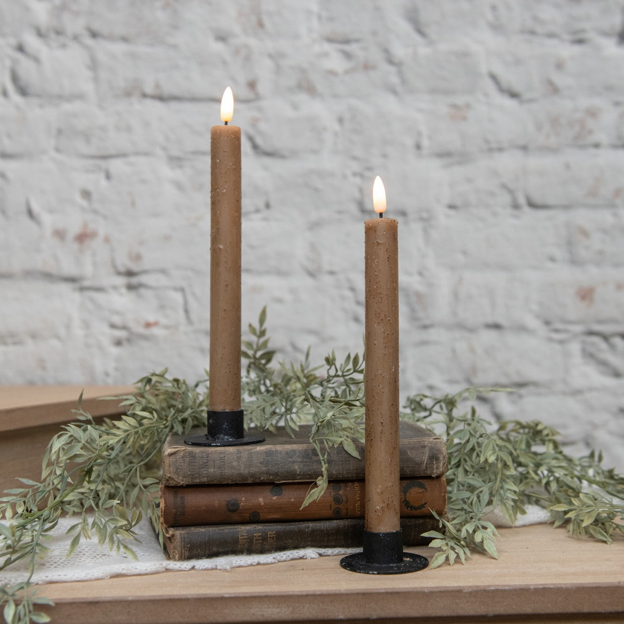 Elegant 3D flame beige taper candles on black holders, styled with vintage books and greenery. Ideal for cozy and rustic home decor settings.