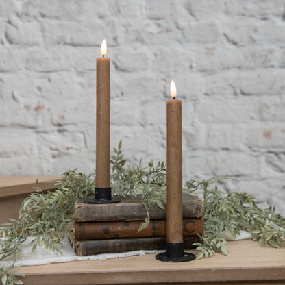 Elegant 3D flame beige taper candles on black holders, styled with vintage books and greenery. Ideal for cozy and rustic home decor settings.