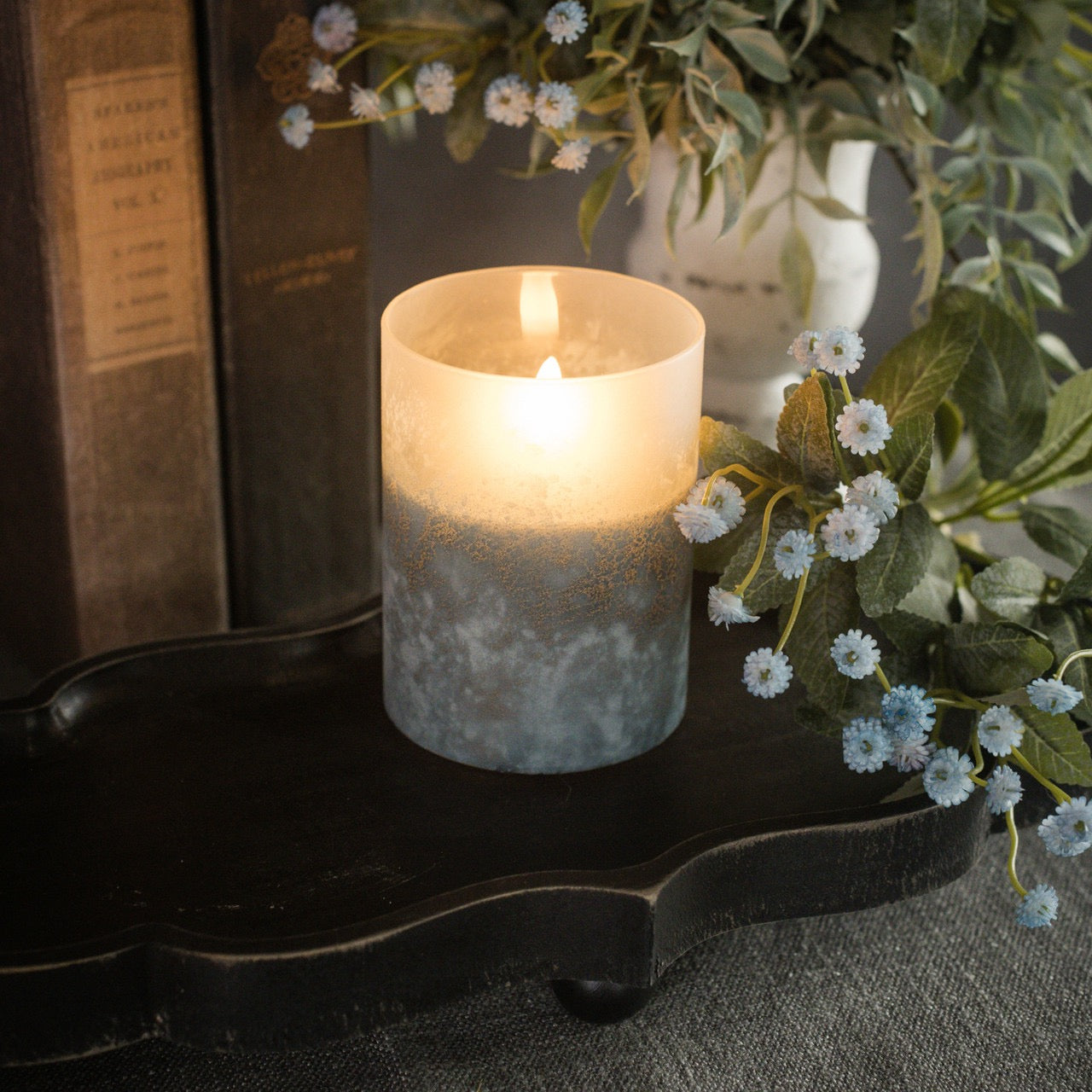 Blue frosted glass 3D flame candle on a decorative shelf, surrounded by books and flowers. Creates a cozy and elegant atmosphere.