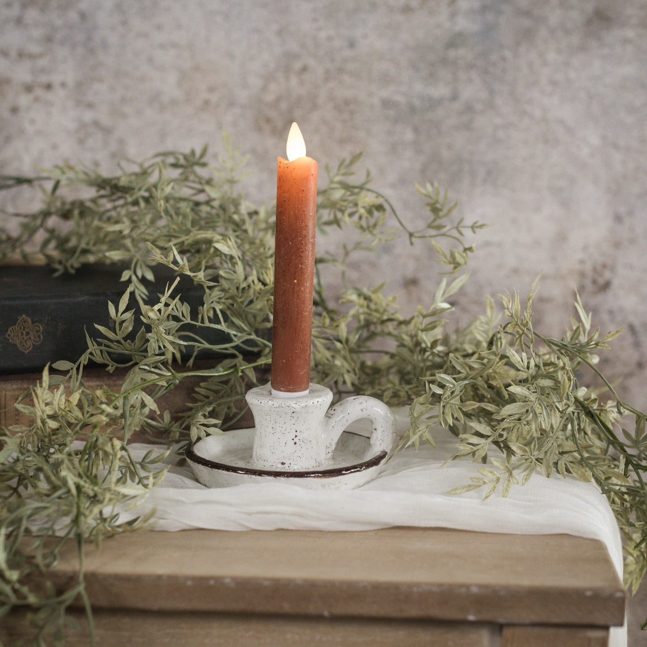 Rustic brown and white taper candle holder with handle, crafted from terracotta. Features a speckled white glaze and earthy brown rim for vintage charm.