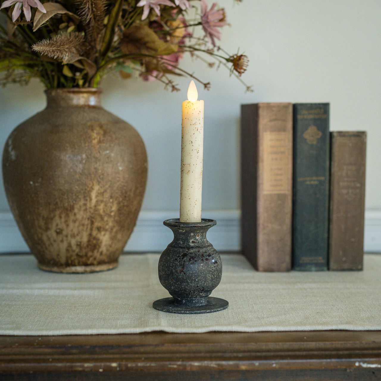 3.5-inch Jasper taper candle holder displayed on a table with a lit candle, complementing a cozy home setting with books and a vase.