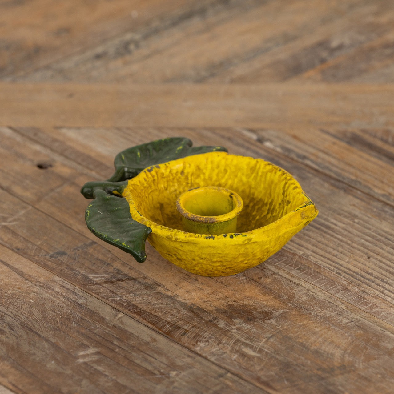 Close-up of a lemon-shaped taper candle holder made of textured yellow metal with green leaves, designed for a single candle, perfect for rustic decor.