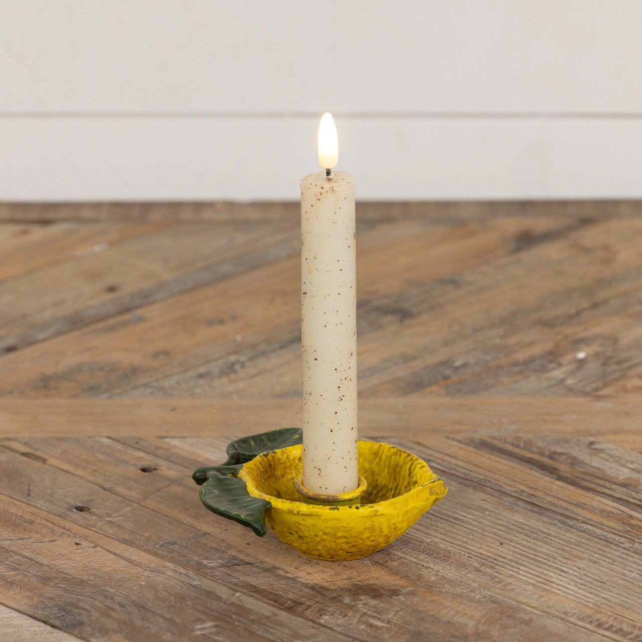 Lemon taper candle holder with a lit candle, featuring a rustic yellow metal design with green leaves, adding a citrus-inspired charm to home decor.