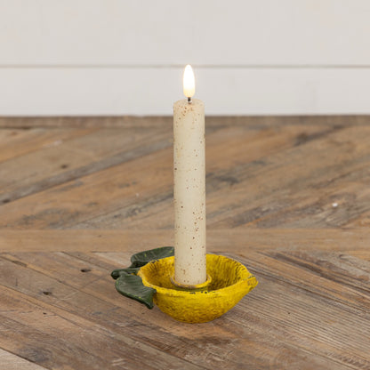 Lemon taper candle holder with a lit candle, featuring a rustic yellow metal design with green leaves, adding a citrus-inspired charm to home decor.