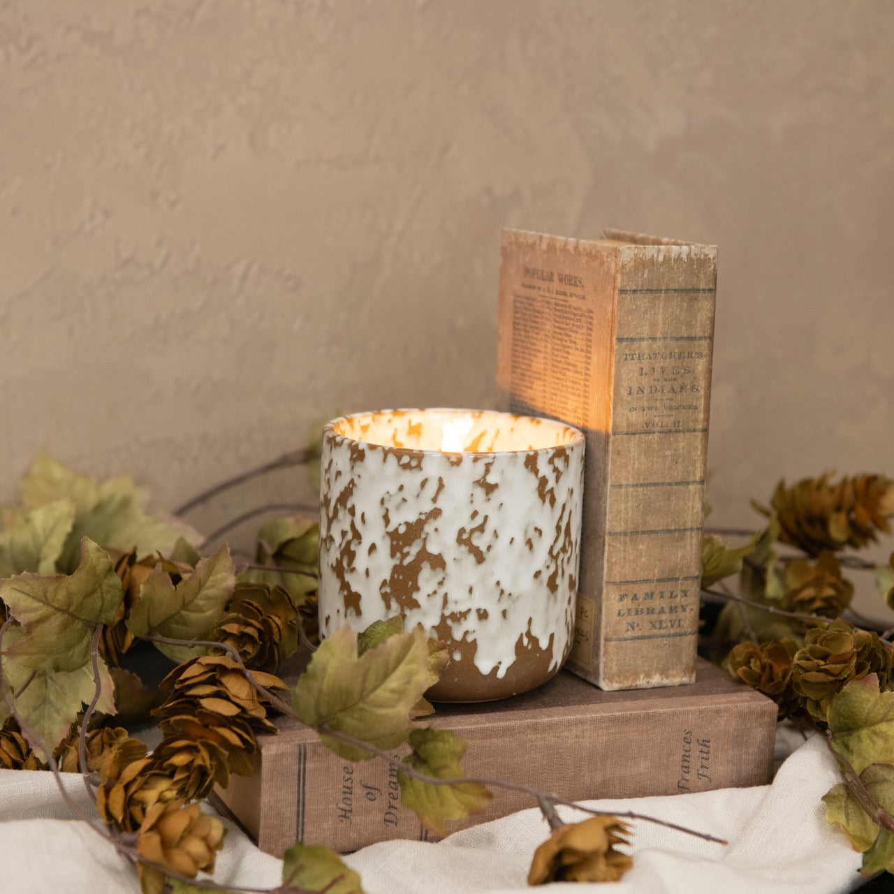 Elegant 3D flame tan ceramic candle with a speckled design, placed among vintage books and autumn decor. A stylish flameless candle for cozy interiors.