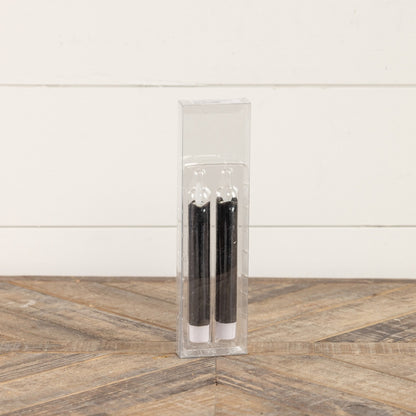 Packaged set of two 6.75-inch black taper candles with moving flame effect in a clear plastic case. Perfect for gifting or home decoration.