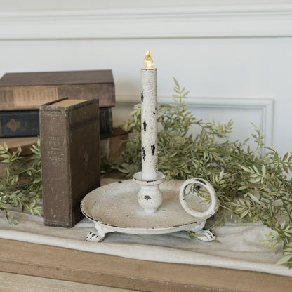 Rustic white metal dish taper candle holder with distressed finish, featuring a round base, handle, and clawfoot design. Perfect for vintage-inspired decor.