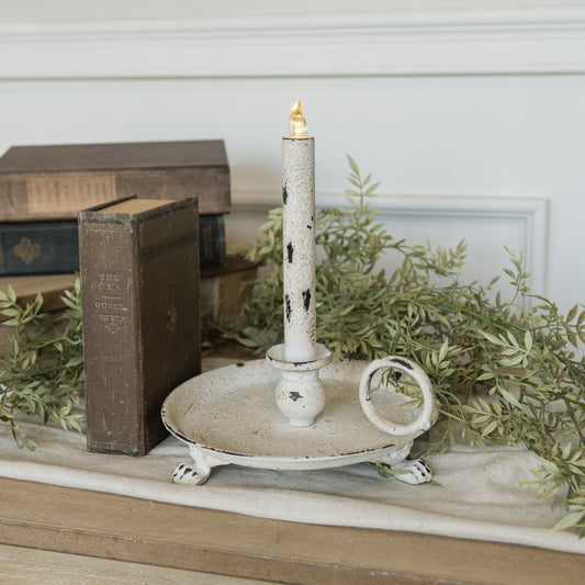 Rustic white metal dish taper candle holder with distressed finish, featuring a round base, handle, and clawfoot design. Perfect for vintage-inspired decor.