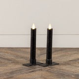 Set of two 6.75-inch black taper candles with moving flame effect, placed on a wooden surface. Ideal for home decor and ambient lighting.