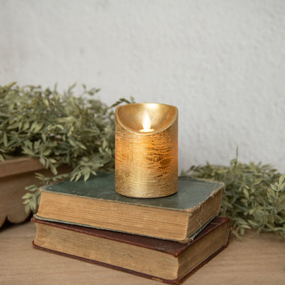 Gold pillar moving flame LED candle placed on stacked vintage books with greenery. A stylish flameless candle for cozy home decor.