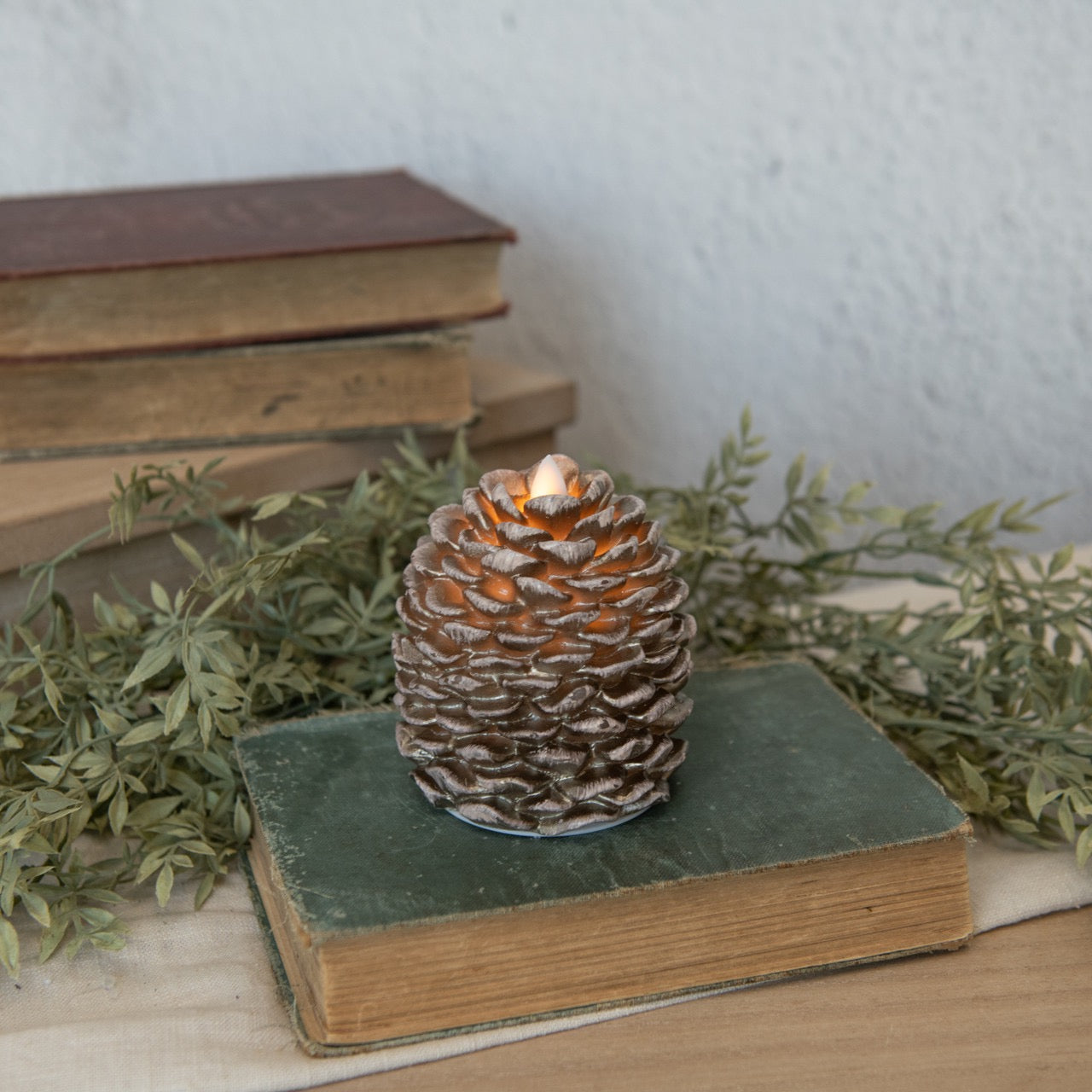 Flameless Moving Flame Pinecone Candle - 4.25" resting on vintage books, adding a warm and natural touch to home decor.