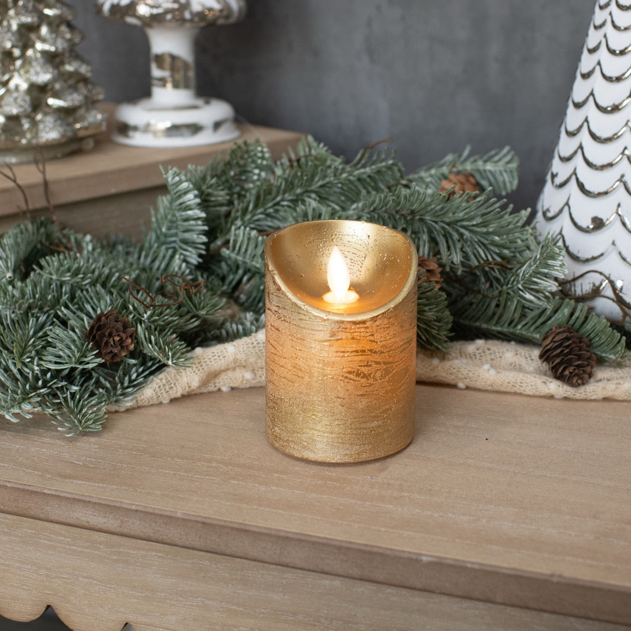 Elegant gold pillar moving flame LED candle on a festive mantel with pine greenery. A safe and stylish addition to holiday decorations.