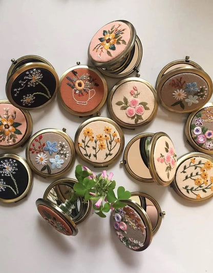 Collection of floral embroidered compact mirrors from Quince Fables, featuring intricate hand-stitched designs on fabric covers.