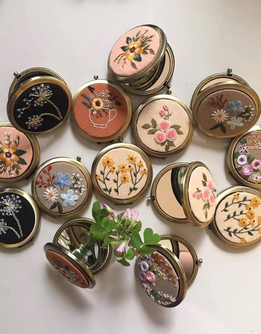 Collection of floral embroidered compact mirrors from Quince Fables, featuring intricate hand-stitched designs on fabric covers.