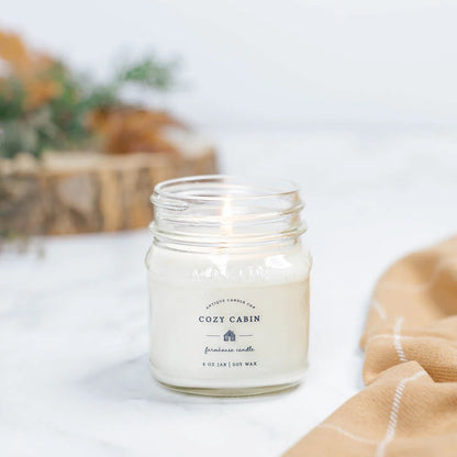 Antique Candle Co Cozy Cabin soy wax candle in an 8oz glass jar. A warm, woodsy scent perfect for a relaxing ambiance.