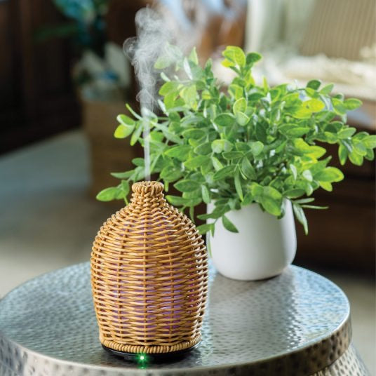 Wicker Vase Ultra Sonic Diffuser emitting mist on a table, enhancing home ambiance. Elegant rattan design complements modern and rustic interiors.