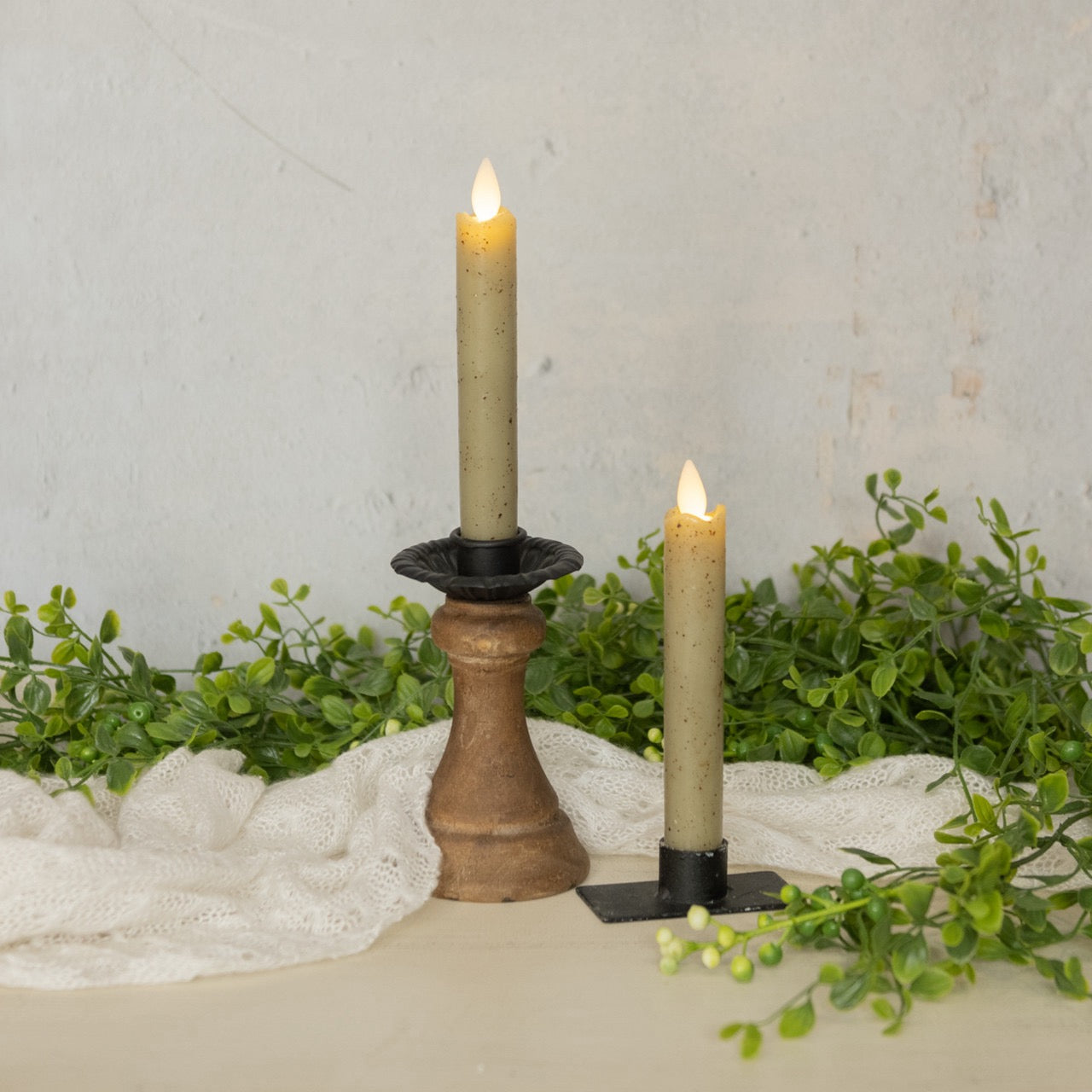 Moving flame green taper candles in decorative holders, surrounded by greenery and fabric, creating a cozy home decor setting.