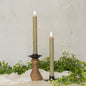 Set of two 9.5-inch green taper candles with realistic 3D flame, displayed in black and wooden candle holders with greenery decor.