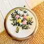 Floral embroidered compact mirror from Quince Fables, showcasing a bouquet of pink and yellow flowers on a cream fabric cover.