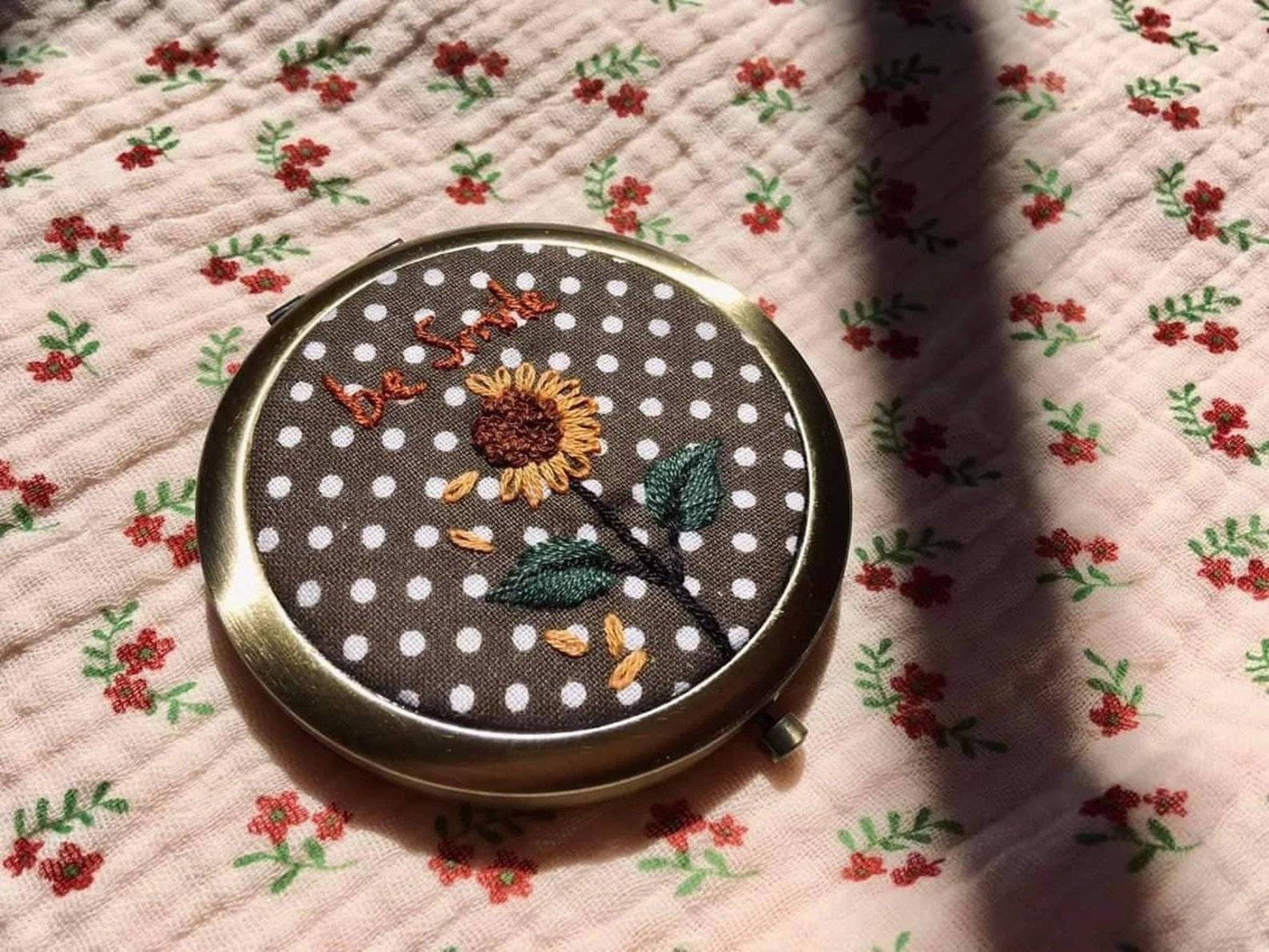 Sunflower-themed floral embroidered compact mirror from Quince Fables with 'be kind' text on a polka dot fabric cover.