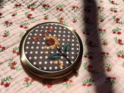 Sunflower-themed floral embroidered compact mirror from Quince Fables with 'be kind' text on a polka dot fabric cover.
