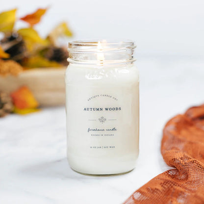 Antique Candle Co 16oz 'Autumn Woods' soy candle burning beside fall leaves and a cozy scarf. Natural soy wax with a warm seasonal fragrance.