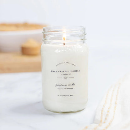 Antique Candle Co 16oz 'Warm Caramel Crumble' soy candle burning beside a dessert dish. Sweet, comforting home fragrance with natural soy wax.